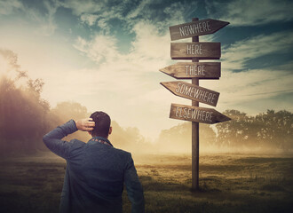 Lost and confused businessman in front of a signpost showing impossible directions. Business dilemma and difficult choice concept. Choosing the correct way on the road sign - obrazy, fototapety, plakaty