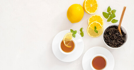 two white cups of tea, black tea brewing, dried tea leaves, fresh mint leaves, lemons whole and pieces, top view, tea drinking, breakfast, ceremony