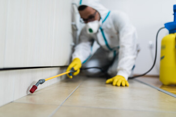 Exterminator in work wear spraying pesticide with sprayer. Selective focus.