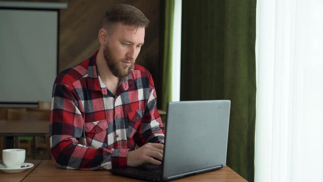 caucasian male using laptop computer, sitting at table in home office, typing on keyboard and looking at screen, enjoying remote work, selective focus.