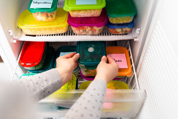 Woman placing container with frozen vegetables in freezer.