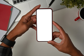 Top view close up of a young man sitting in the office using a touchscreen on a smartphone with a blank white screen, for business and technology concept.