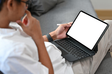 Close up of a young Asian man working on a tablet with a white blank screen, for business, education, home and technology concept.