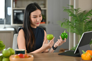 A portrait of a young pretty Asian woman choosing fruits and preparing a meal, having a tablet to look at a recipe, for food, health and cooking concept.