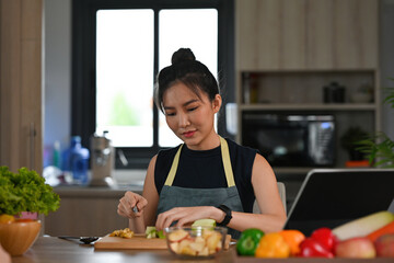 A portrait of a young pretty Asian woman chopping fruits and preparing a meal on a wooden cut board, for food, health and cooking concept.