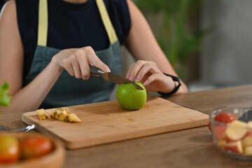 Cropped view young woman's hands chopping green apple and fruits preparing a meal on a wooden cut board, for food, health and cooking concept.