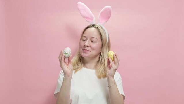 4k. Happy easter. Beautiful girl in Easter bunny ears holding painted easter eggs on pink background going to celebrate Easter, stands over pink studio background. Spring holiday concept