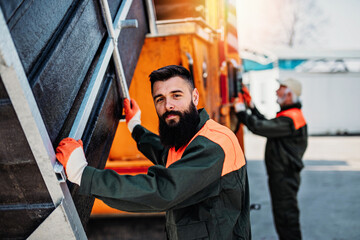 Senior and young garbage men working together on emptying dustbins for trash removal..