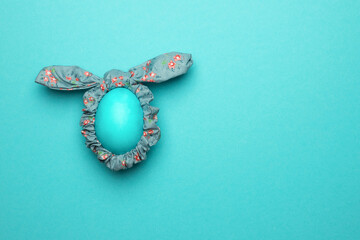 Ears of the Easter bunny are made of a hair band with an egg on a blue background. The concept of an Easter card in a minimalist style.