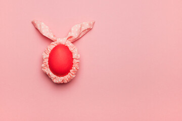 Ears of the Easter bunny are made of a hair band with an egg on a pink background. The concept of an Easter card in a minimalist style.