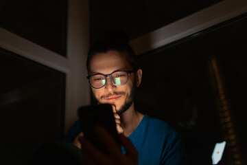 Night portrait of young smiling man with smartphone in hand.