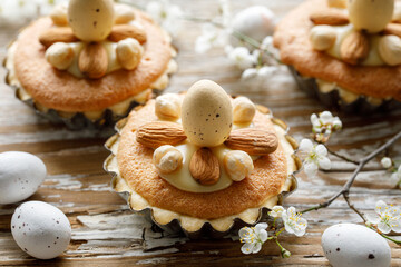 Easter mini cupcakes with almond frangipane cream and white chocolate on a rustic wooden table decorated with spring flowers, close up view. An idea for an Easter delicious dessert