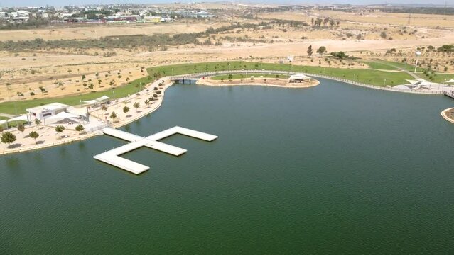 Flying over the artificial lake in the park with Beer Sheva buildings at background