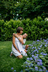 Smiling mother and son are walking in the park together in summer in light clothes. Soft sunset light.