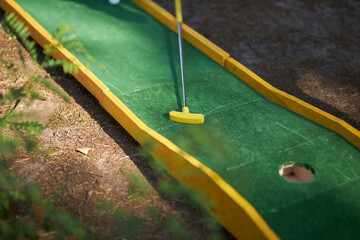 mini golf in nature. minigolf player with white sneakers putting golf ball into the hole on bumpy green lane. 