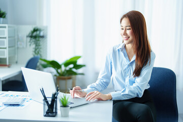 An Asian entrepreneur or businesswoman shows a smiling face while working with using computer on a wooden table.