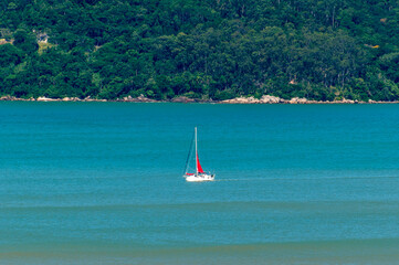 Obraz premium Boat sailing on the blue sea of Balneário Camboriú Brazil with a forest in the background.