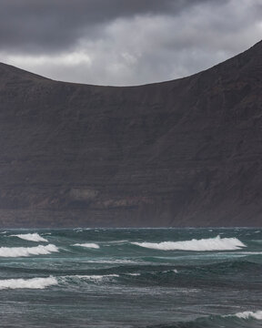 View of Ocean waves rolling on the beach along the shoreline with mountains in background in Caleta de Famara, Lanzarote, Canary Islands, Spain.