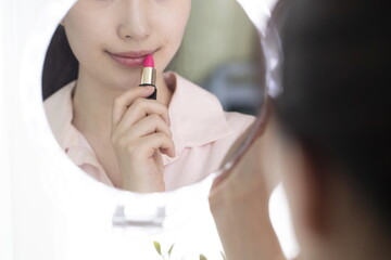 Young woman applying lipstick in mirror