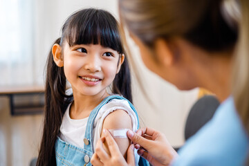 Childhood vaccination. Asian young woman doctor vaccinating little girl at home. Vaccine for...