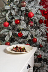 Pieces of stewed beef with cherries in a plate against the background of a decorated Christmas tree