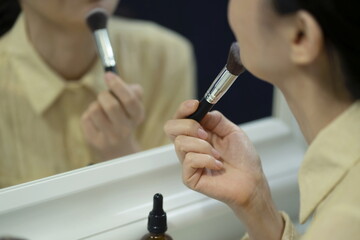 Obraz na płótnie Canvas Woman applying make-up in mirror, using brush, close-up