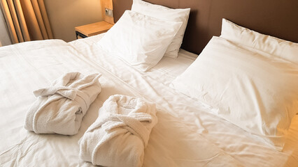 2 snow-white bath robes, beautifully folded, lie on a bed covered with white linen.