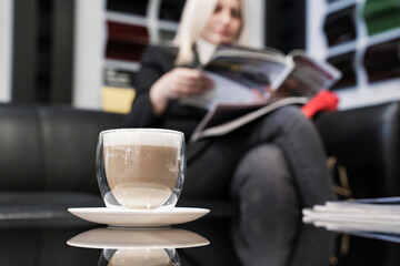 Girl in a car dealership drinks coffee and reads the press. Close-up of coffee.