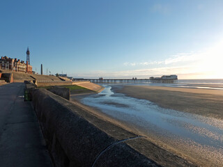 view of blackpool tower and south pier from the promenade with town buildings in afternoon sunlight