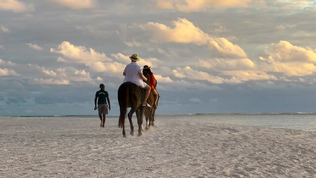 Horseback riding on a tropical beach along the coast of Ocean. Horse riders move against the backdrop of turquoise water and sunset