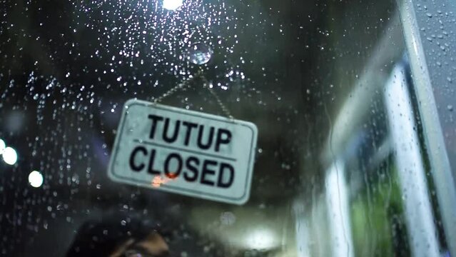 Open-closed board in the cafe pasted on the glass door at night and it's raining outside