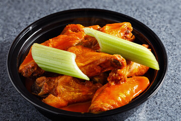 Chicken wings covered in sauce with celery sticks in a plastic carry-out container