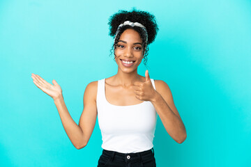 Young latin woman isolated on blue background holding copyspace imaginary on the palm to insert an ad and with thumbs up