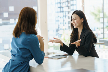 Obraz premium Two young attractive asian business woman in the conversation, exchanging ideas at work.