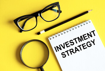Investment Strategy text written on a notebook with glasses, magnifying glass and pencil