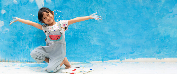 Banner of asian little girl is painting the blue color on the wall and she look happy and funny,...