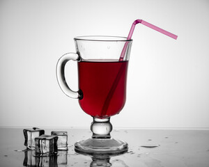 Cold tea, cocktail, fruit drink in a tall glass cup with a drinking straw on a table with pieces of ice on a light gray gradient