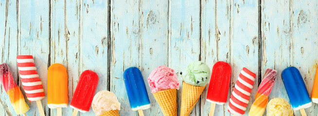 Variety of colorful summer popsicles and ice cream treats. Top view bottom border on a rustic blue...