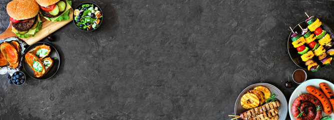 Summer BBQ or picnic food double corner border. Selection of burgers, grilled meat, vegetables, fruits, salad and potatoes. Overhead view on a dark banner background. Copy space.