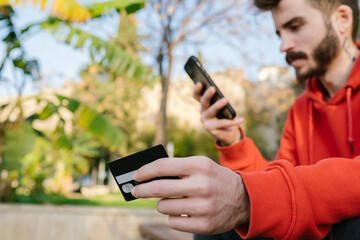 Credit card, young man shopping online holding credit card, he has completed his payment and is trying to find out the duration of his order.