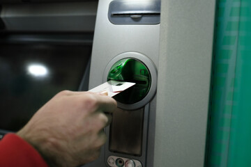 Naklejka premium Card entry, a young man inserting his card into the card slot of the ATM, pin security and automatic teller