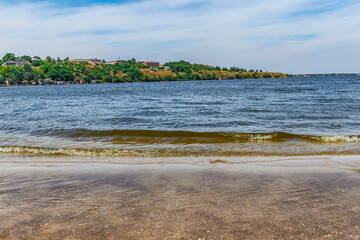 Waves on the Inhul River on Strilka beach in Mykolaiv, Ukraine. Blue water close-up and urban coastline on the horizon