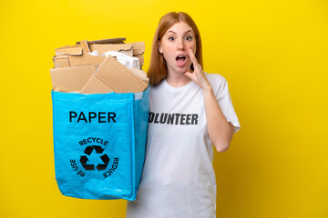 Young redhead woman holding a recycling bag full of paper to recycle isolated on yellow background with surprise and shocked facial expression