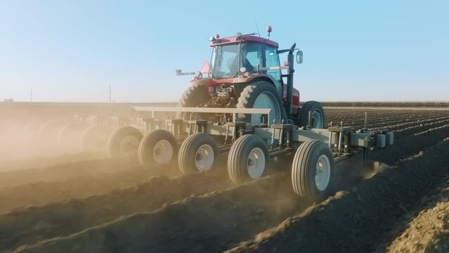 Agricultural machine with heavy blades cuts a furrow for sowing seeds. Aerial view of a tractor plowing the terrain, leaving shallow ditches on land. High quality 4k footage