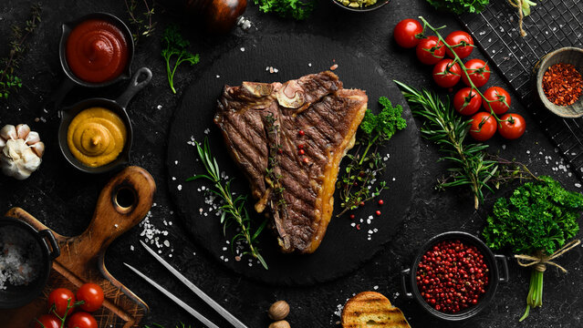 porterhouse steak or T Bone Steak dry aged of beef Ready to Cook on wooden Board with herbs, pepper and salt. On a black stone background.