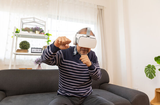 Senior man using VR headset to explore augmented reality at home in living room . Disabled elderly male playing virtual online game, having fun with modern technologies. - Powered by Adobe