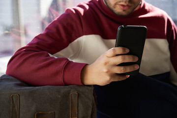 boy's hand resting on his backpack consults the mobile phone