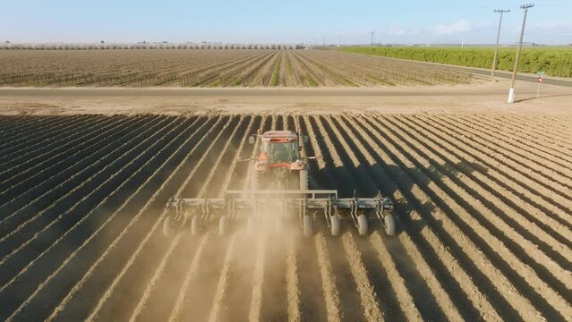 Aerial view of a tractor plowing the terrain, leaving shallow ditches on land. Agricultural machinery cultivating black soil on a farm as seen from above. High quality 4k footage