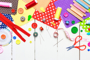 Various fabric, sewing tools and buttons on a white wooden table