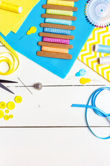 Yellow and blue fabrics, sewing tools and buttons on a white wooden table